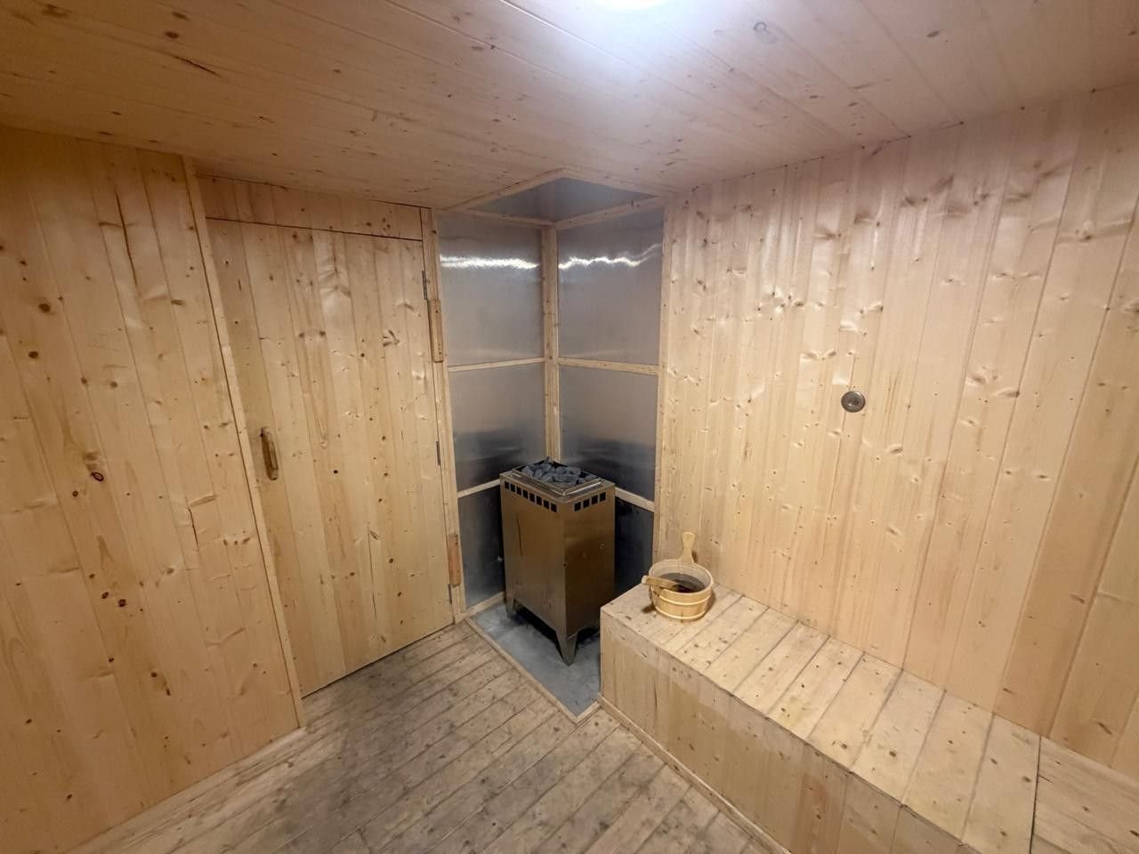 Sauna heater with stones and a wooden bucket beside a pine bench
